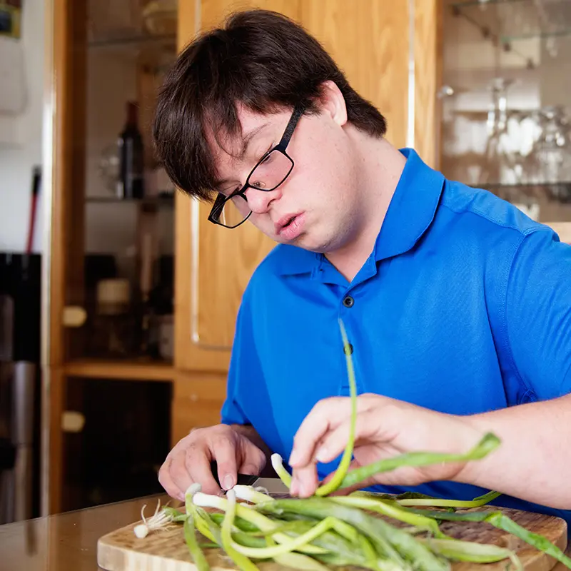 Junger Mann mit Down-Syndrom schneidet Lauchzwiebeln